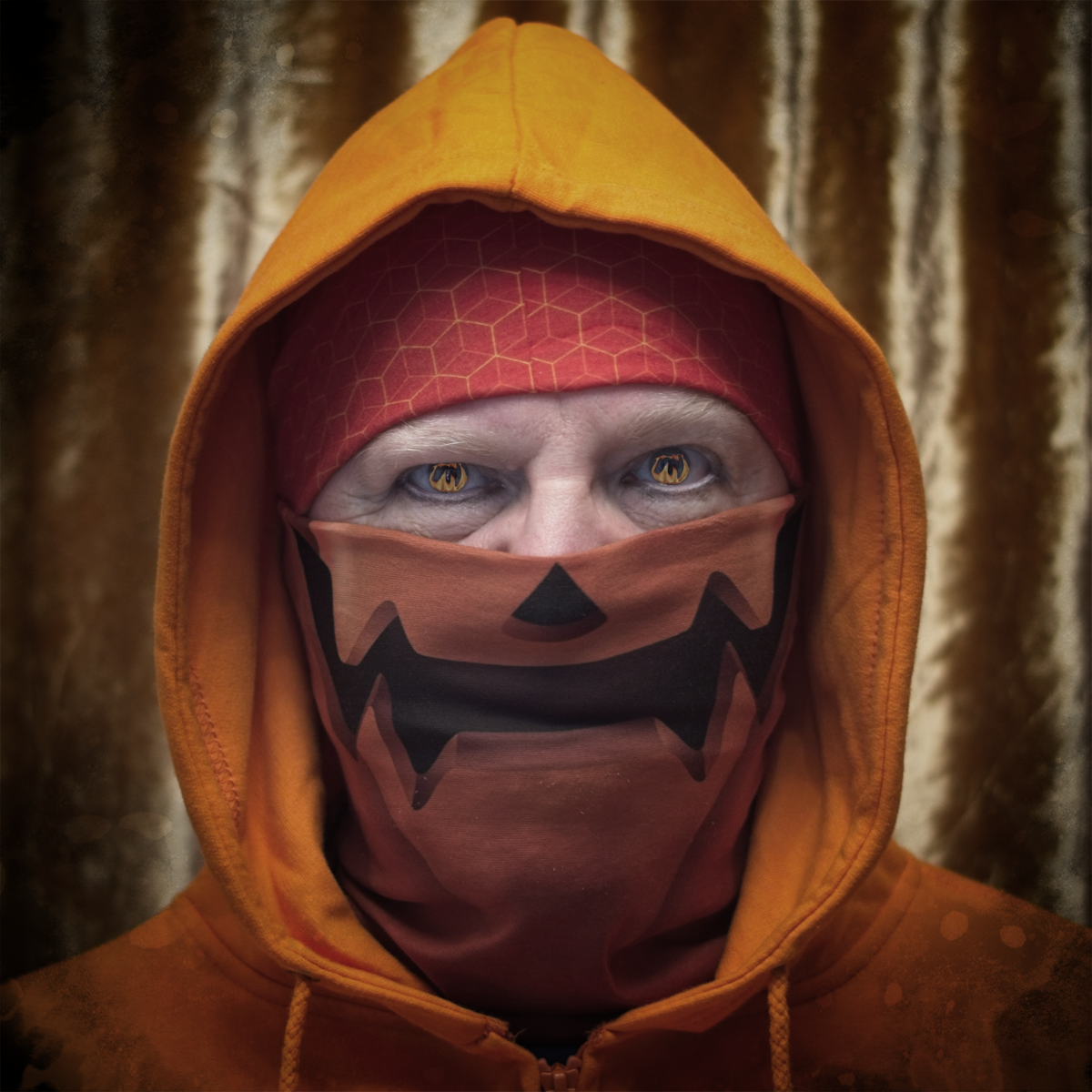 A head shot of Corum Silverhand, wearing a light orange hoodie, with dark orange bandana and a pumpkin-themed face covering. Shown on a golden background.