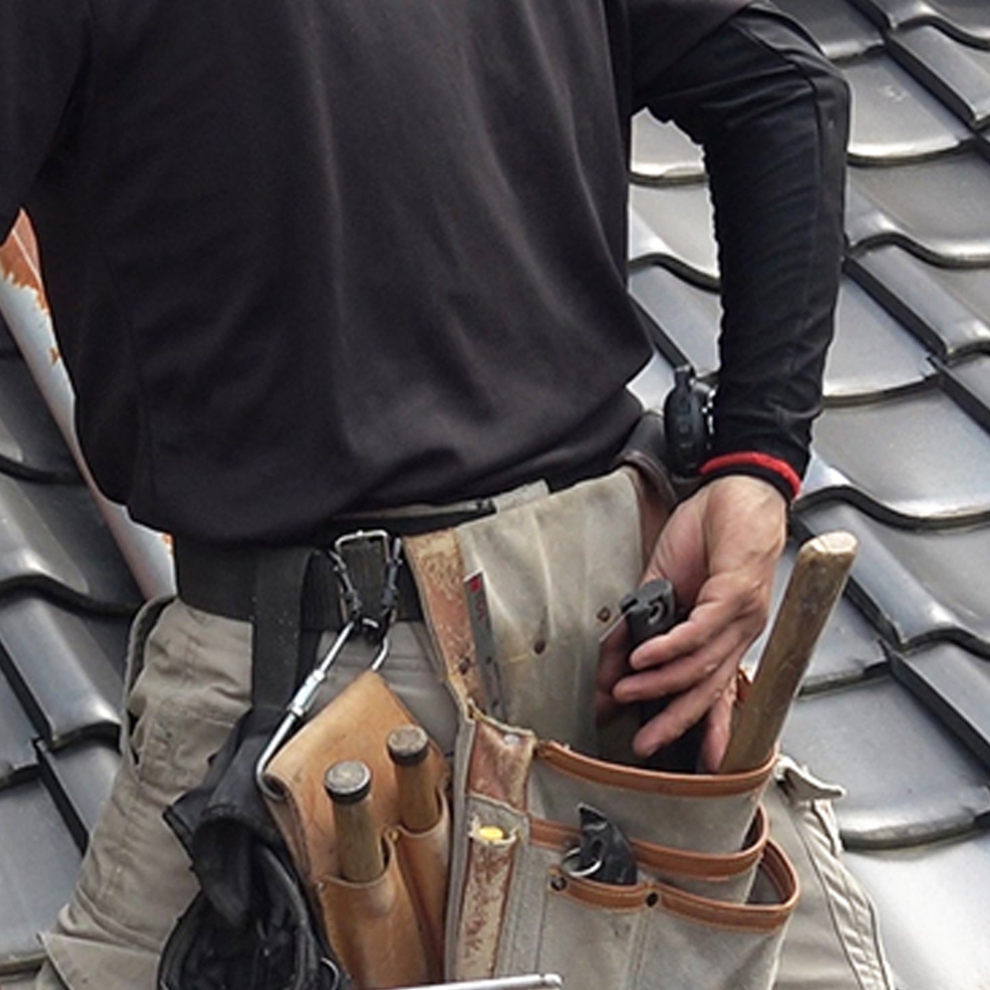 Image of the Zetsaw V Handy200 Daikume Folding Anahiki-nokogiri Japanese Saw being placed into the pouch of a toolbelt of a roofing worker.