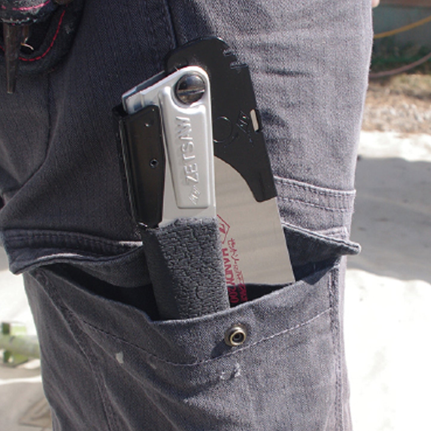 Image of the Zetsaw V Handy200 Daikume Folding Anahiki-nokogiri Japanese Saw folded and placed into the thigh pocket of a construction worker.
